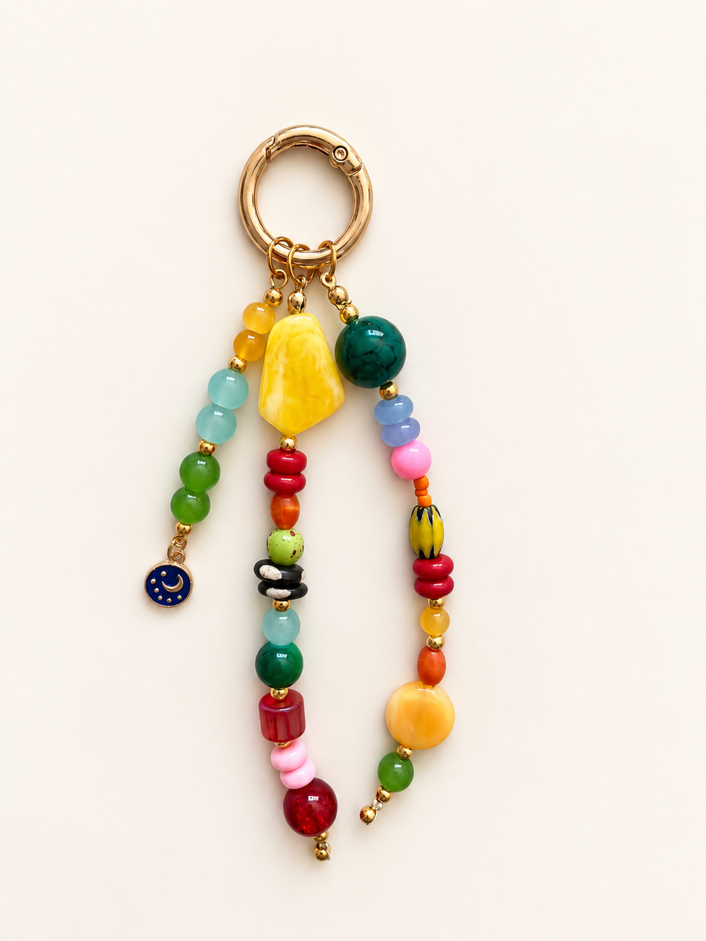 A colorful beaded keychain with a gold-tone split ring, featuring multiple strands of round and irregular beads in green, yellow, red, pink, orange, and blue, accented with small gold beads and a tiny blue moon charm.