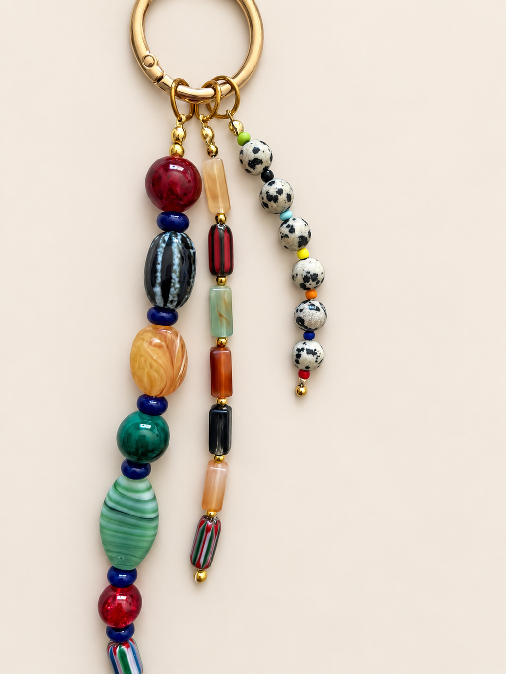 A bohemian-style beaded keychain with a gold-tone split ring, featuring multiple strands of colorful glass beads in red, green, orange, black, white, and blue on a light beige background.