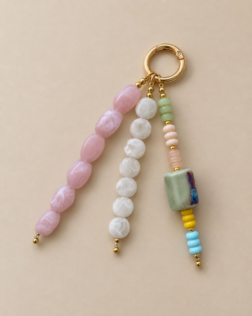 A beaded keychain charm with a gold split ring, featuring three strands of polished beads in pink, white, and light green, with small gold spacer beads and a decorative marbled green square bead.