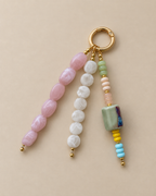 A beaded keychain charm with a gold split ring, featuring three strands of polished beads in pink, white, and light green, with small gold spacer beads and a decorative marbled green square bead.