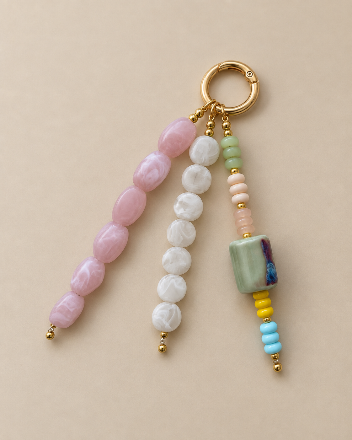 A beaded keychain charm with a gold split ring, featuring three strands of polished beads in pink, white, and light green, with small gold spacer beads and a decorative marbled green square bead.