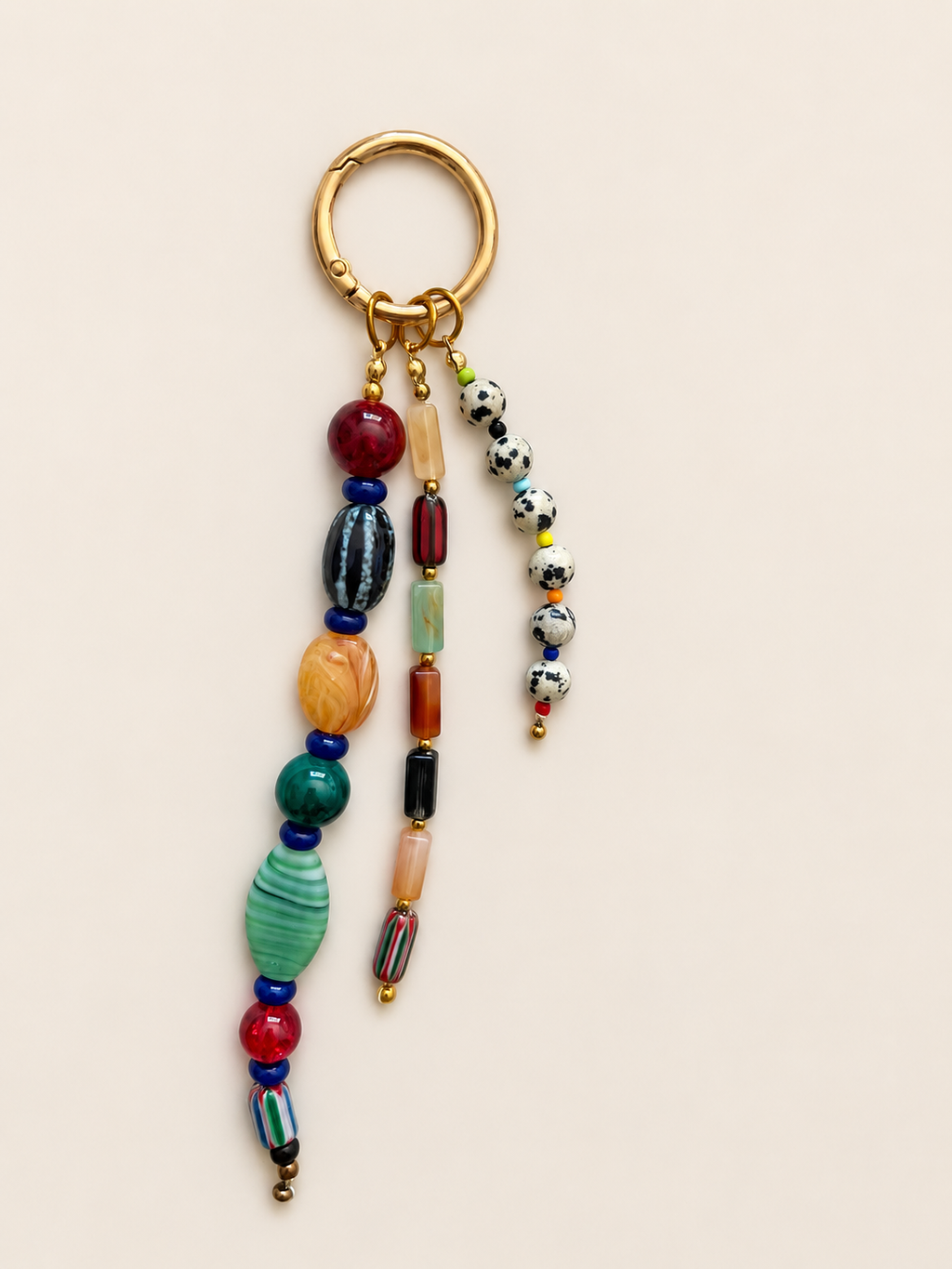 A gold-tone metal keychain with multiple dangling beaded strands in assorted colors, including red, green, blue, orange, black, white, and yellow, shown on a plain beige background.
