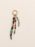 A gold-tone keychain with multiple dangling beaded strands in assorted colors, including green, orange, red, blue, black, and white, shown on a plain beige background.