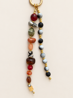 A beaded keychain with a gold-tone split ring, featuring two strands of polished gemstone beads in red, green, orange, brown, black, gray, and yellow on a light beige background.