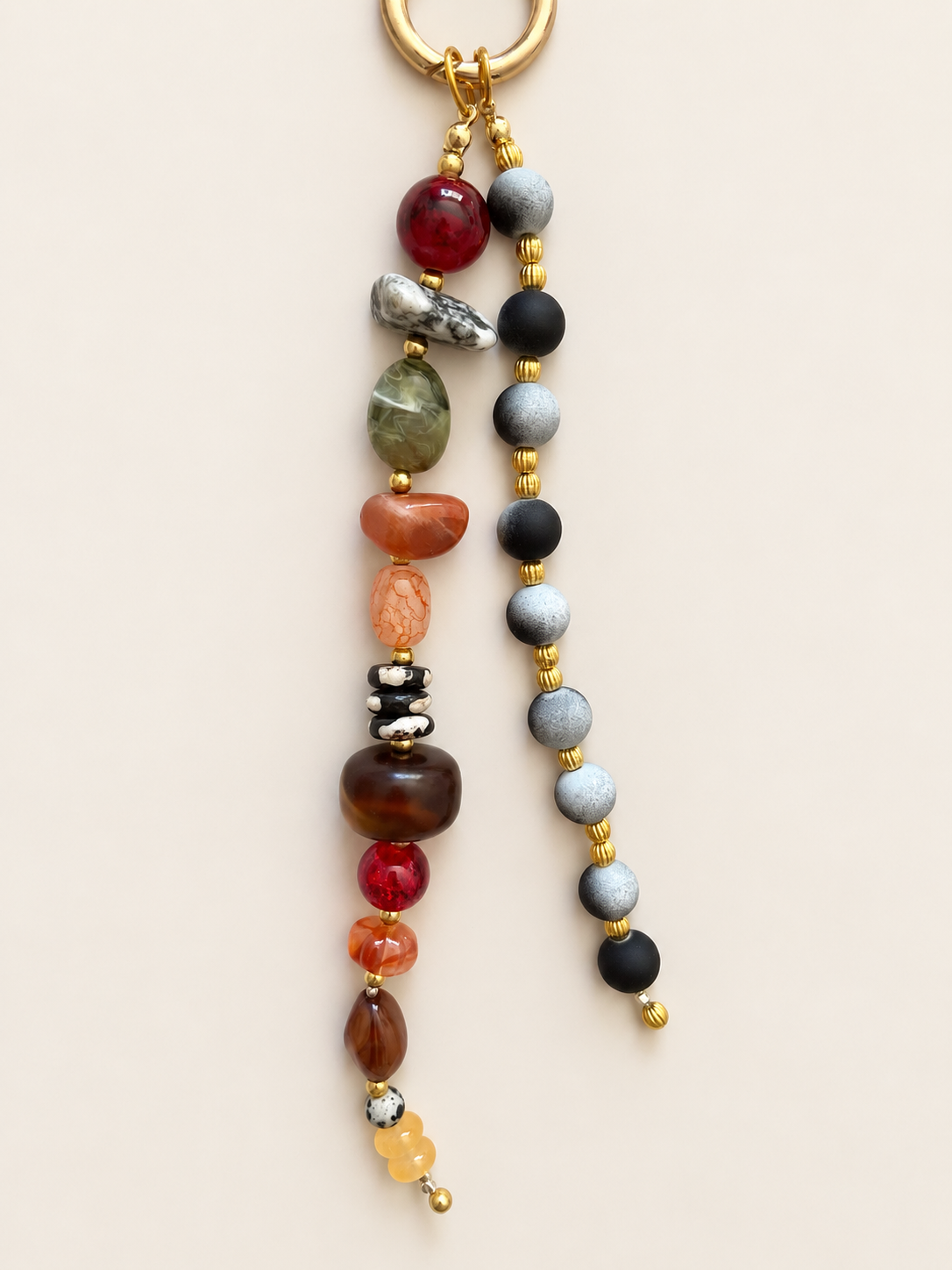 A beaded keychain with a gold-tone split ring, featuring two strands of polished gemstone beads in red, green, orange, brown, black, gray, and yellow on a light beige background.