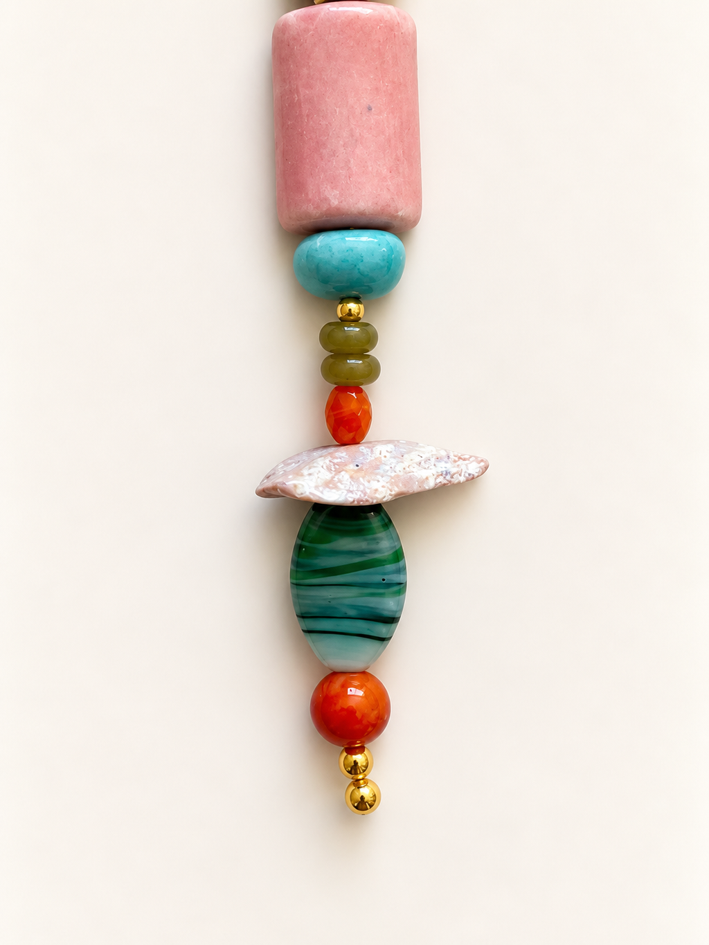 A vertical strand of colorful artisanal beads on a plain off-white background. The set features a large pink cylindrical bead, a turquoise disc, small olive green and orange beads, a textured white shell, a green and blue striped teardrop bead, another orange bead, and small gold spacer beads at the bottom.