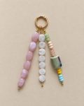 A beaded keychain charm with a gold-tone split ring, featuring three hanging strands of polished beads in pink, white, and pastel green, yellow, and blue on a solid beige background.