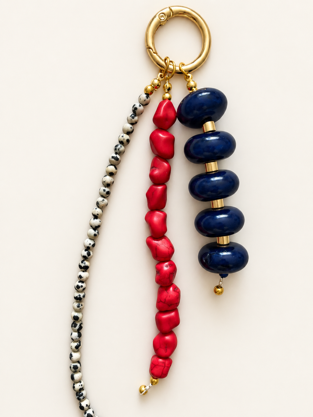 A beaded keychain or bag charm with a gold-tone split ring, featuring three hanging strands: one with dark navy blue beads, one with bright red coral-like beads, and one with small metallic silver and gold spacer beads.