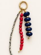 A beaded keychain or bag charm with a gold-tone split ring, featuring three hanging strands: one with dark navy blue beads, one with bright red coral-like beads, and one with small metallic silver and gold spacer beads.