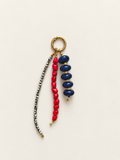 A beaded keychain featuring a gold-tone split ring, a strand of dark blue glossy beads, a strand of bright red heart-shaped beads, and a long strand of small metallic silver beads, all displayed on a light cream background.