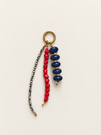 A beaded keychain featuring a gold-tone split ring, a strand of dark blue glossy beads, a strand of bright red heart-shaped beads, and a long strand of small metallic silver beads, all displayed on a light cream background.