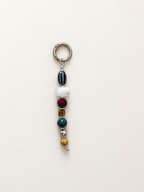 A beaded keychain charm with a silver metal split ring, featuring a series of colorful beads including black, white, burgundy, amber, teal, silver, and gold, set against a plain off-white background.